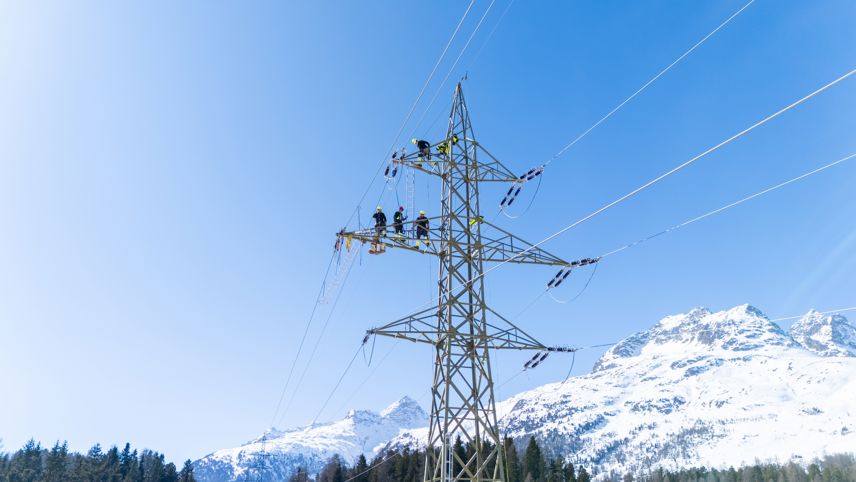 Technicians work on a high-voltage transmission tower, replacing insulators