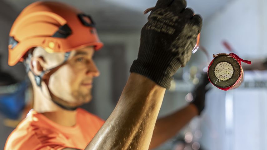 Helmeted worker holds the cross-section of a power cable; further work continues in the background.
