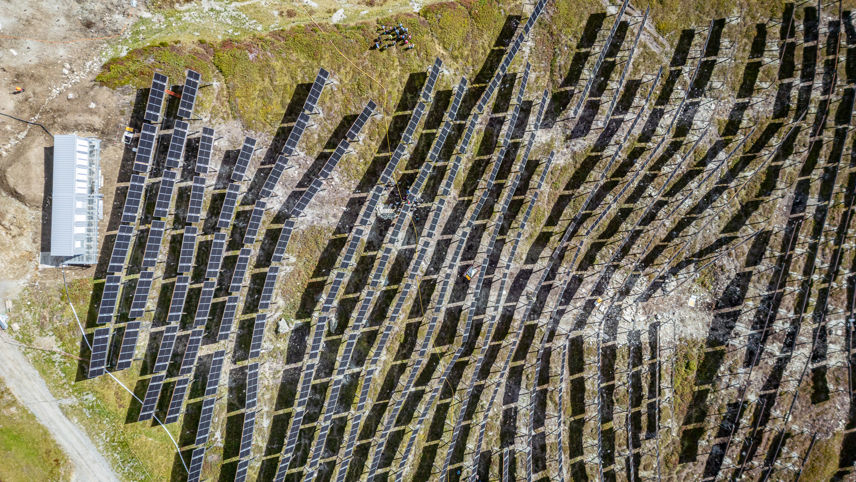 Aerial view of Madrisa Solar: rows of solar panels on an alpine slope with a service building.