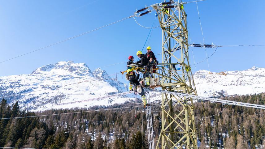Technicians work on a high-voltage pylon replacing insulators