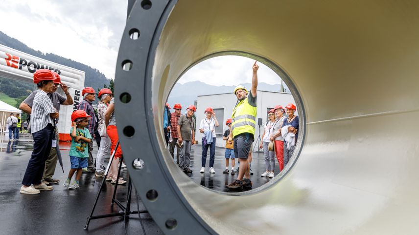 Open day at Robbia power plant: helmeted visitors as a staff member explains the facility through a large pipe.