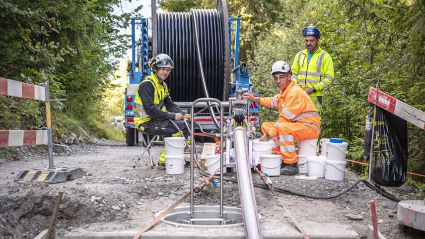 Work crew installs cabling; a large cable drum and equipment set up on a forest road.